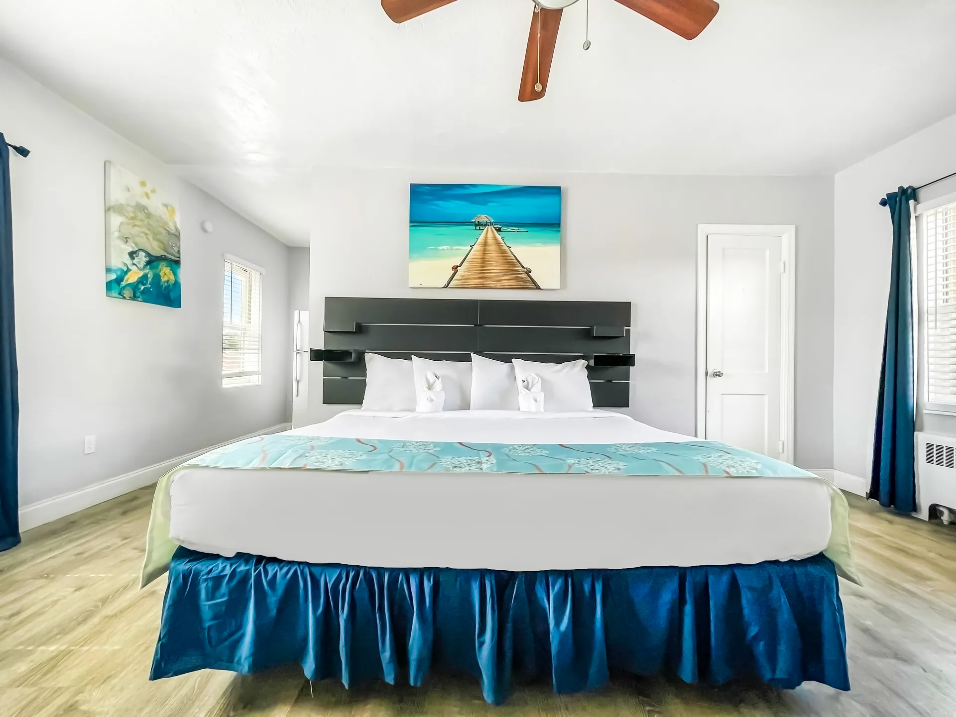 A wide view of a hotel room with a large bed, blue accents, and beach-themed artwork.