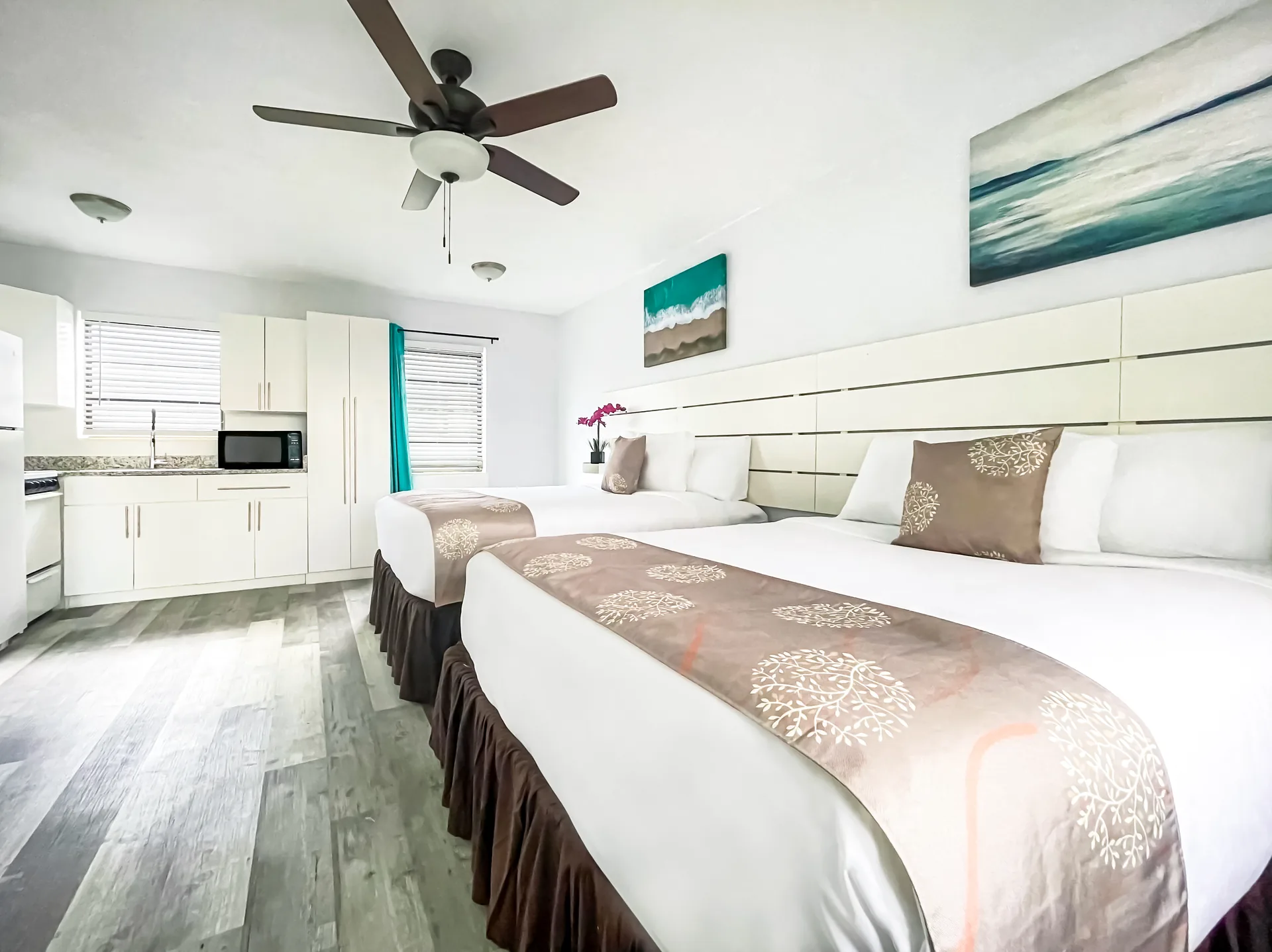 A hotel suite with two beds, a kitchenette, and artwork on the walls.