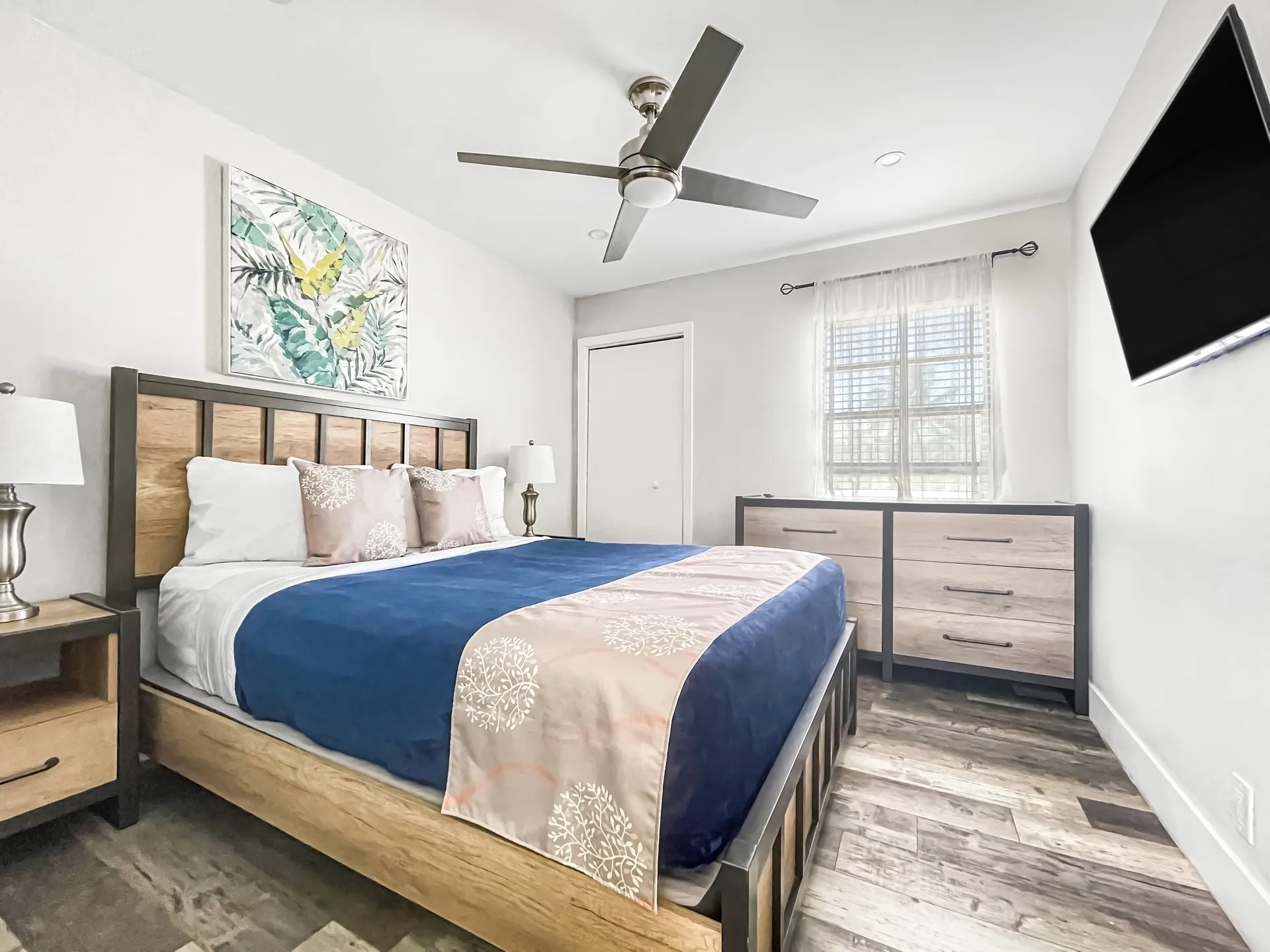 A clean and modern guest room with a large bed, dresser, and TV.