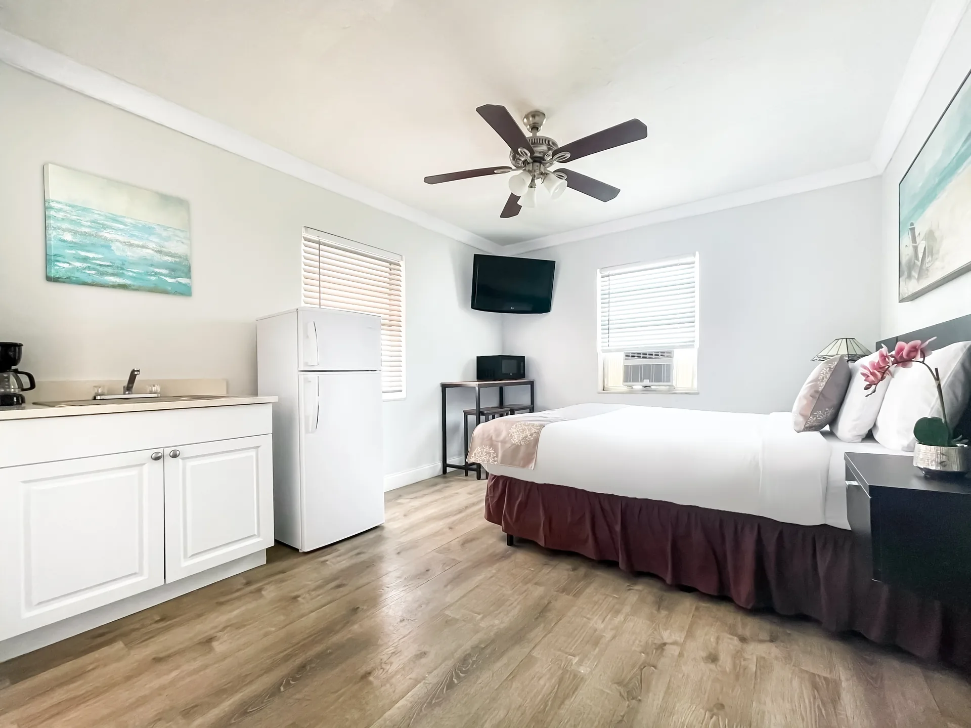 A hotel room with a kitchenette, bed, TV, and ceiling fan.
