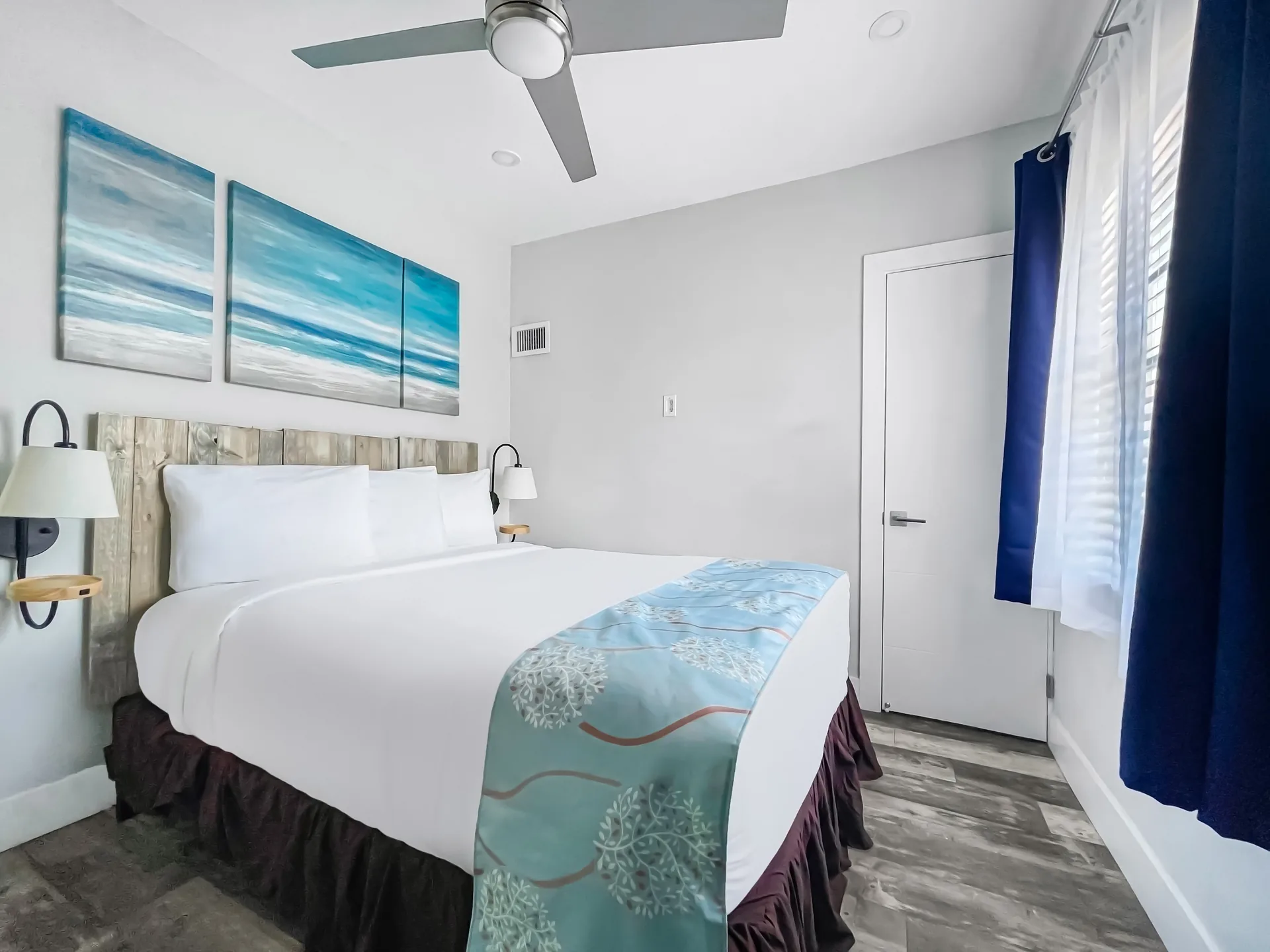 A hotel room with a bed, ceiling fan, door, and window