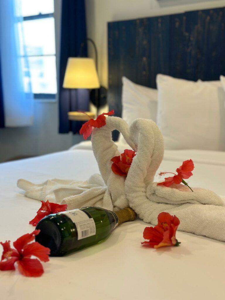 Fancy towel folding magic: Two crafted towel swans on the bed with flowers and prosecco 