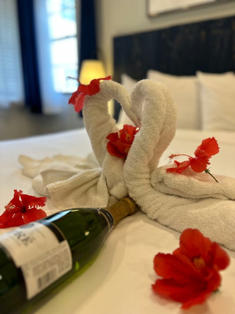 Fancy towel folding magic: Two crafted towel swans on the bed with flowers and prosecco 